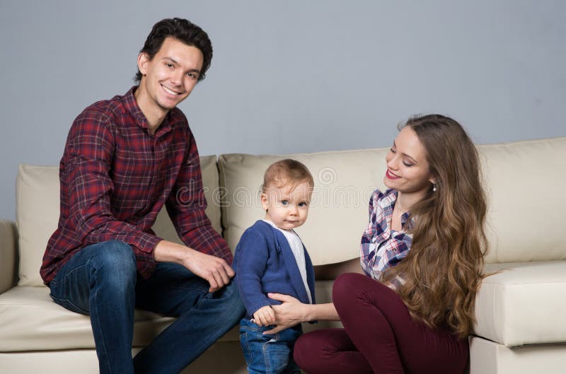 Famiglia con un bambino in una stanza con un sofà immagine stock Famiglia con un bambino in una stanza con un sofà immagine stock