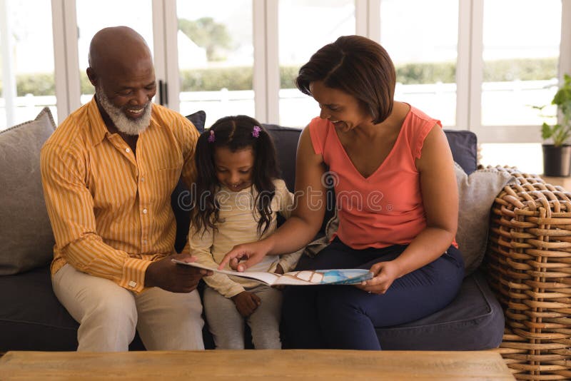 Famiglia di diverse generazioni che legge un libro di storia in salone immagini stock Famiglia di diverse generazioni che legge un libro di storia in salone immagini stock