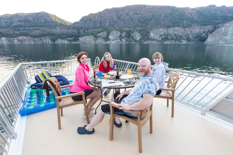 Famiglia di quattro felice che si siede insieme esterno in un lago che mangia cena immagine stock libera da diritti Famiglia di quattro felice che si siede insieme esterno in un lago che mangia cena immagine stock libera da diritti
