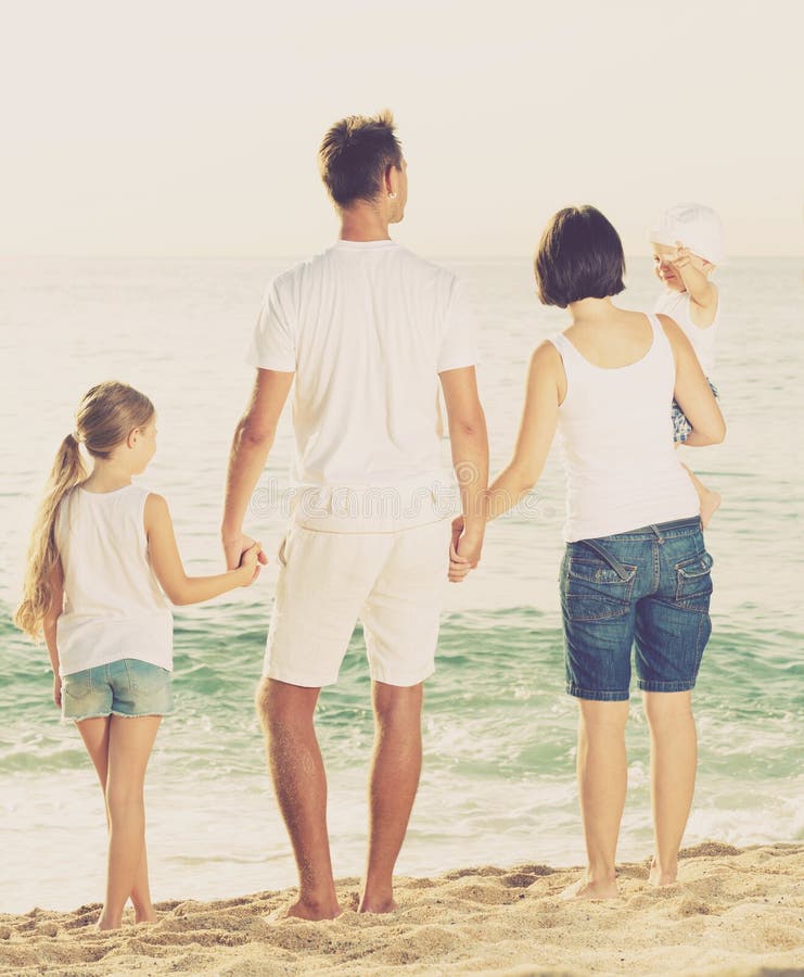 Famiglia di quattro felice che sta con di andata posteriore immagine stock Famiglia di quattro felice che sta con di andata posteriore immagine stock
