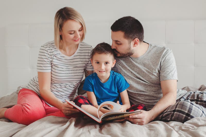 Famiglia di tre persone che si siede sul letto in libro di lettura della camera da letto fotografia stock libera da diritti Famiglia di tre persone che si siede sul letto in libro di lettura della camera da letto fotografia stock libera da diritti