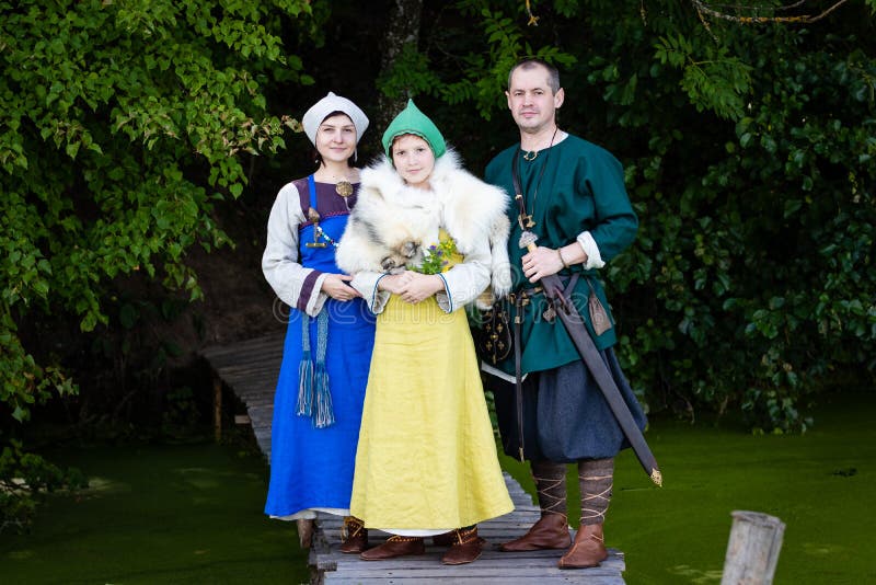 Famiglia di Viking sui passaggi pedonali di legno dal lago donna, uomo e ragazza in vestiti antichi dell'età di vichingo immagini stock Famiglia di Viking sui passaggi pedonali di legno dal lago donna, uomo e ragazza in vestiti antichi dell'età di vichingo immagini stock