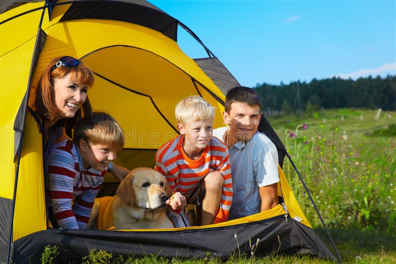 Family outdoor portrait of smiling mother, two boys, young man and labrador looking happy outside of tent. Family outdoor portrait of smiling mother, two boys, young man and labrador looking happy outside of tent