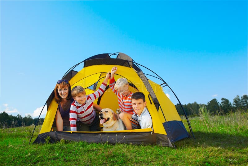 Family outdoor portrait of smiling mother, two boys, young man and labrador looking happy outside of tent. Family outdoor portrait of smiling mother, two boys, young man and labrador looking happy outside of tent