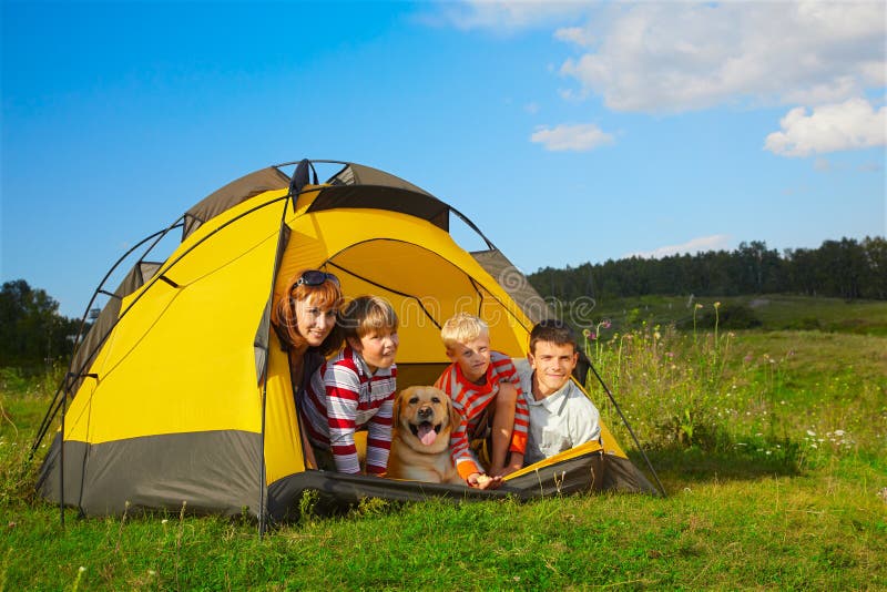 Family outdoor portrait of smiling mother, two boys, young man and labrador looking happy outside of tent. Family outdoor portrait of smiling mother, two boys, young man and labrador looking happy outside of tent