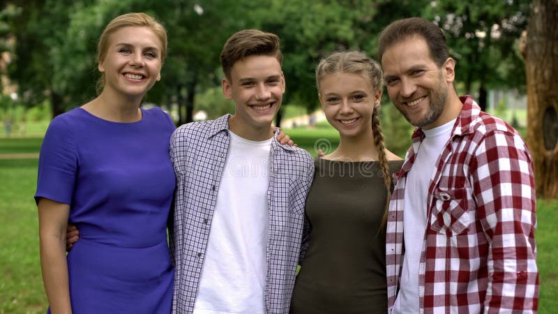 Famiglia felice che abbraccia e che sorride nel parco, posante nella macchina fotografica, orgoglio per i bambini immagine stock libera da diritti Famiglia felice che abbraccia e che sorride nel parco, posante nella macchina fotografica, orgoglio per i bambini immagine stock libera da diritti