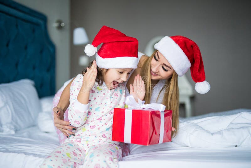 Famiglia felice che porta i cappelli di Santa Claus che si siedono sul letto Generi l'elasticità ed il regalo sorpreso di Santa d fotografia stock Famiglia felice che porta i cappelli di Santa Claus che si siedono sul letto Generi l'elasticità ed il regalo sorpreso di Santa d fotografia stock