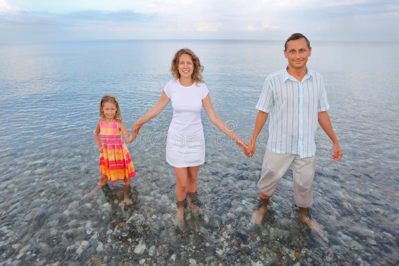 Famiglia felice che si leva in piedi ginocchio-profonda in mare sulla spiaggia fotografia stock Famiglia felice che si leva in piedi ginocchio-profonda in mare sulla spiaggia fotografia stock