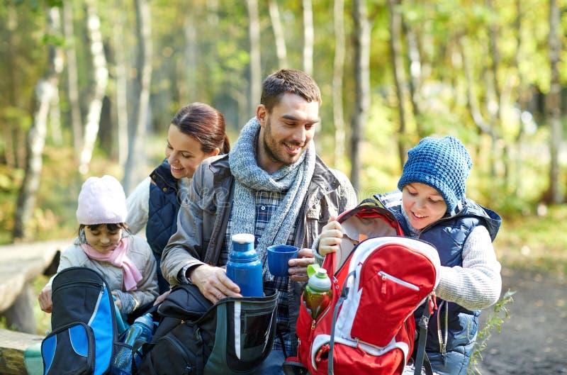 Camping, travel, tourism, hike and people concept - happy family with backpacks and thermos at camp. Camping, travel, tourism, hike and people concept - happy family with backpacks and thermos at camp