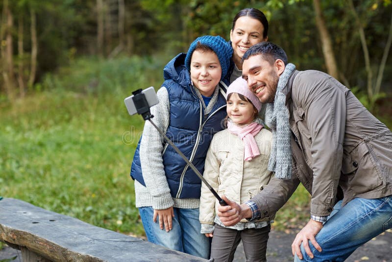 Camping, tourism, hike, technology and people concept - happy family taking picture with smartphone on selfie stick at camp. Camping, tourism, hike, technology and people concept - happy family taking picture with smartphone on selfie stick at camp