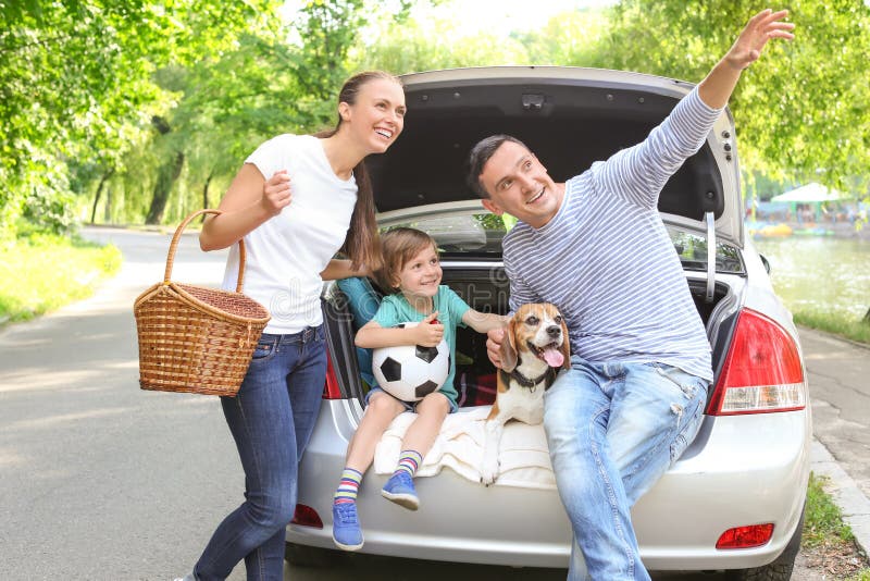Famiglia felice con il cane sveglio vicino all'automobile all'aperto fotografia stock Famiglia felice con il cane sveglio vicino all'automobile all'aperto fotografia stock