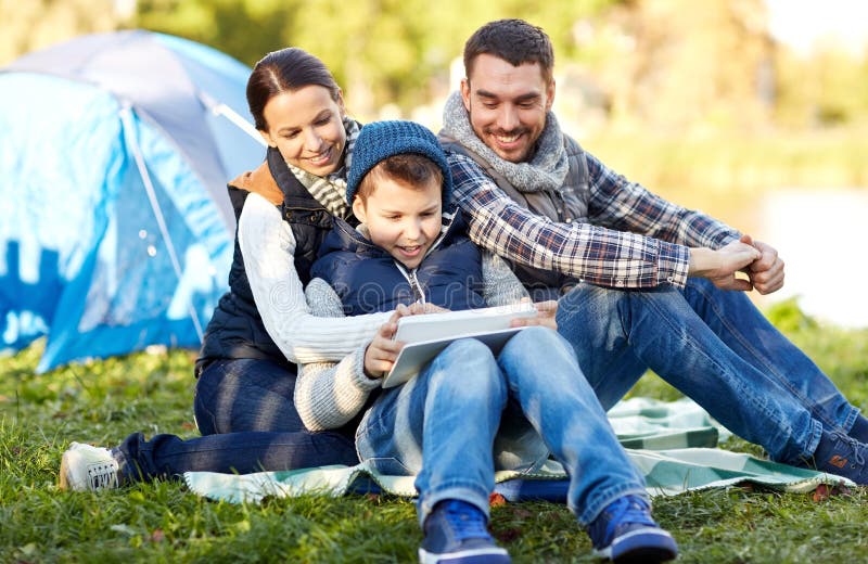 Camping, tourism, hike, technology and people concept - happy family with tablet pc computer and tent at camp site. Camping, tourism, hike, technology and people concept - happy family with tablet pc computer and tent at camp site