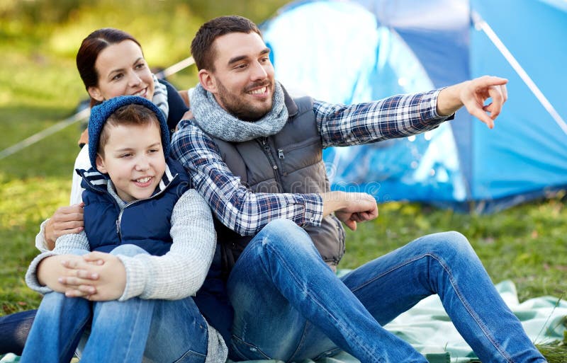 Camping, tourism, hike and people concept - happy family over tent at camp site pointing finger to something. Camping, tourism, hike and people concept - happy family over tent at camp site pointing finger to something