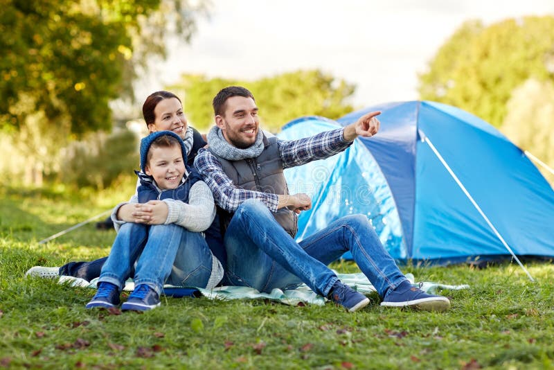 Camping, tourism, hike and people concept - happy family over tent at camp site pointing finger to something. Camping, tourism, hike and people concept - happy family over tent at camp site pointing finger to something