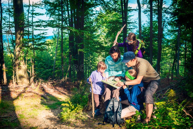 Famiglia felice - padre, madre e figlie - su un viaggio della montagna nella foresta che esamina la mappa fotografia stock Famiglia felice - padre, madre e figlie - su un viaggio della montagna nella foresta che esamina la mappa fotografia stock