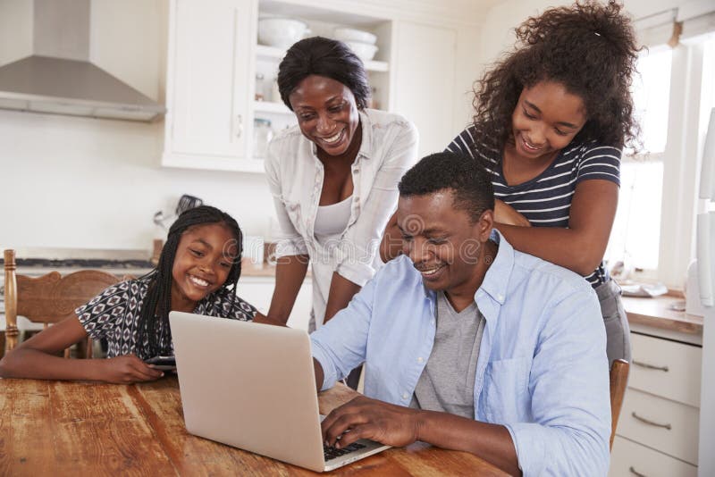 Family Around Kitchen Table Booking Vacation On Laptop Together. Family Around Kitchen Table Booking Vacation On Laptop Together