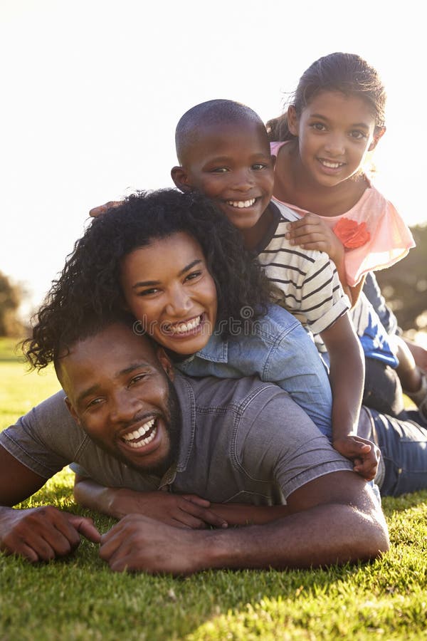 Famiglia nera felice che si trova in un mucchio su erba all'aperto fotografia stock libera da diritti Famiglia nera felice che si trova in un mucchio su erba all'aperto fotografia stock libera da diritti
