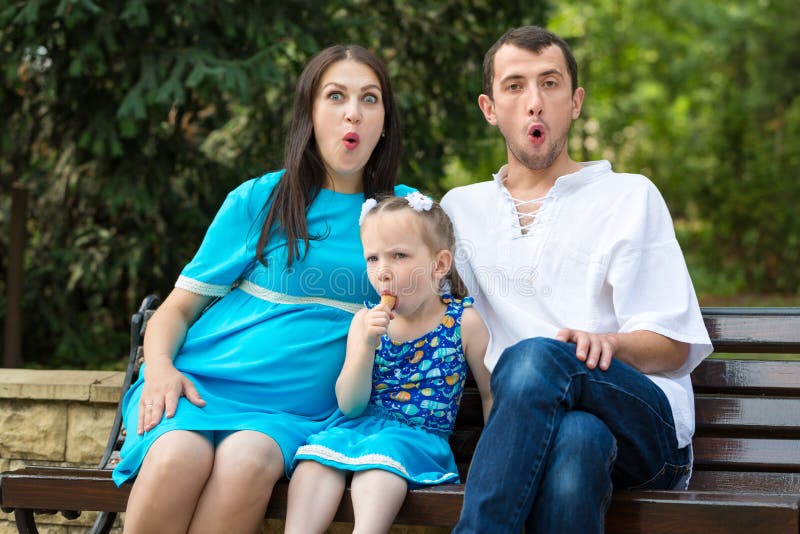 Famiglia seduta su una panchina nel parco. Una bambina che mangia una tazza di waffel. Donna incinta. concetto di vita familiare f fotografia stock libera da diritti Famiglia seduta su una panchina nel parco. Una bambina che mangia una tazza di waffel. Donna incinta. concetto di vita familiare f fotografia stock libera da diritti