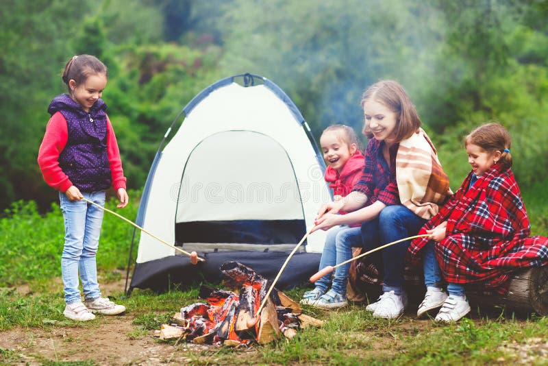 Happy tourist family on a journey hike. mother and children fry sausages on bonfire near the tent. Happy tourist family on a journey hike. mother and children fry sausages on bonfire near the tent