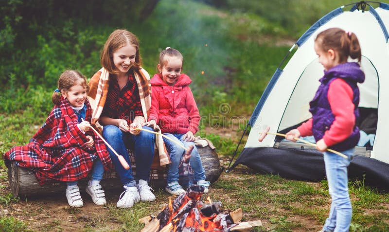 Happy tourist family on a journey hike. mother and children fry sausages on bonfire near the tent. Happy tourist family on a journey hike. mother and children fry sausages on bonfire near the tent