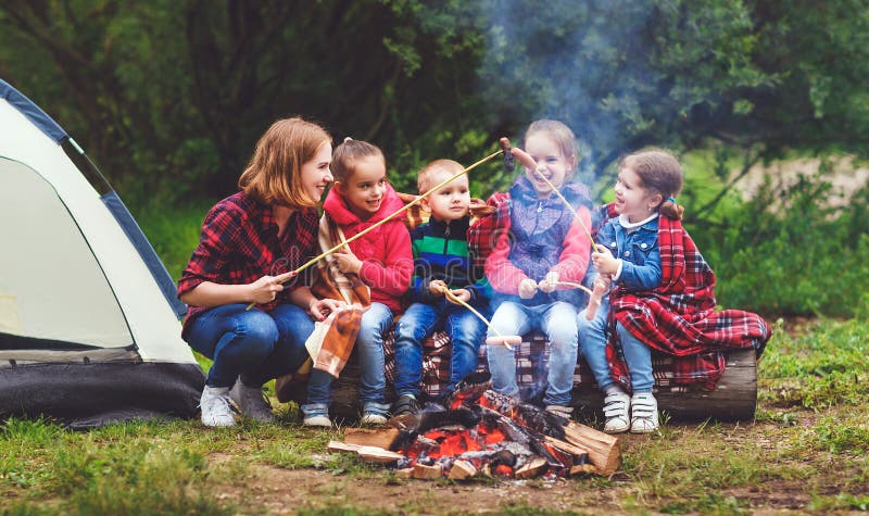 Happy tourist family on a journey hike. mother and children fry sausages on bonfire near the tent. Happy tourist family on a journey hike. mother and children fry sausages on bonfire near the tent