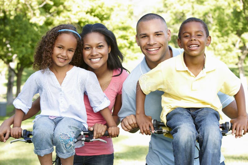 Familia afroamericana joven que completa un ciclo en parque foto de archivo Familia afroamericana joven que completa un ciclo en parque foto de archivo