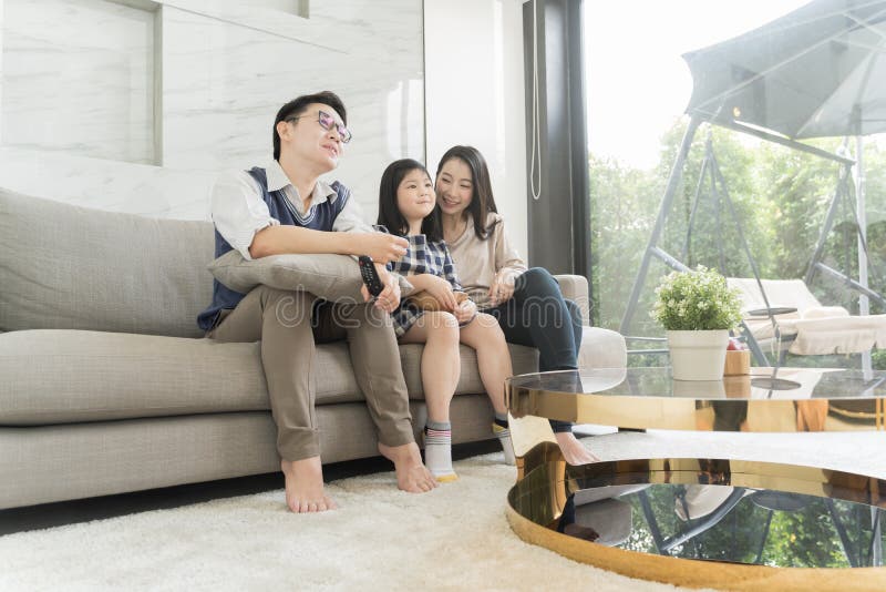 Familia asiática feliz que ve la TV junto en el sofá en sala de estar Familia y concepto casero imagenes de archivo