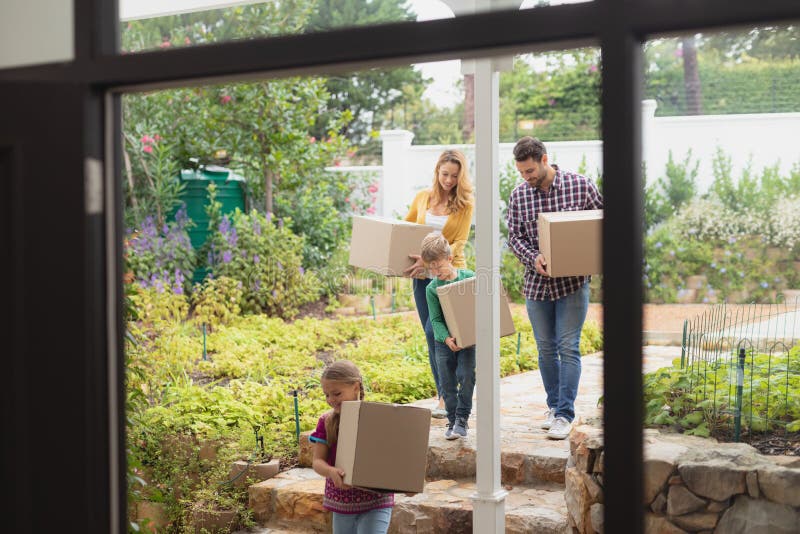 Familia caucásica feliz con las cajas de cartón que camina hacia hogar imagen de archivo Familia caucásica feliz con las cajas de cartón que camina hacia hogar imagen de archivo