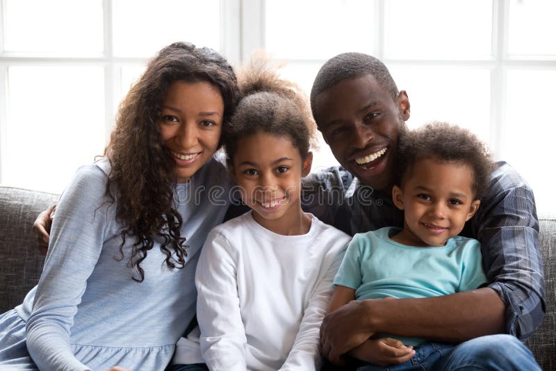 Familia de cuatro miembros negra feliz que mira la cámara en casa