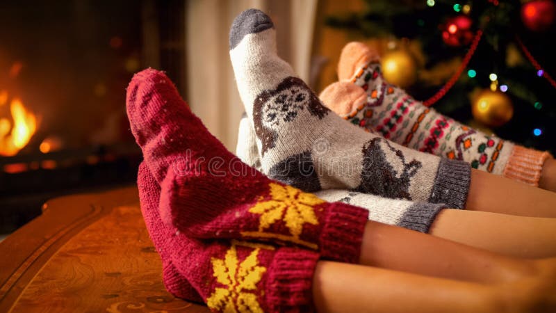 Family in woolen socks holding feet on table next to burning fireplace and Christmas tree. Family in woolen socks holding feet on table next to burning fireplace and Christmas tree