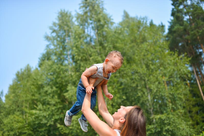 Familia feliz al aire libre la madre lanza al bebé para arriba, riendo y jugando en verano en la naturaleza fotos de archivo Familia feliz al aire libre la madre lanza al bebé para arriba, riendo y jugando en verano en la naturaleza fotos de archivo