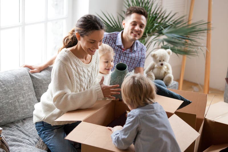 Happy family with two kids unpacking boxes after relocation moving into or settling in new home concept, excited small children helping parents with belongings sitting on sofa in living room together. Happy family with two kids unpacking boxes after relocation moving into or settling in new home concept, excited small children helping parents with belongings sitting on sofa in living room together