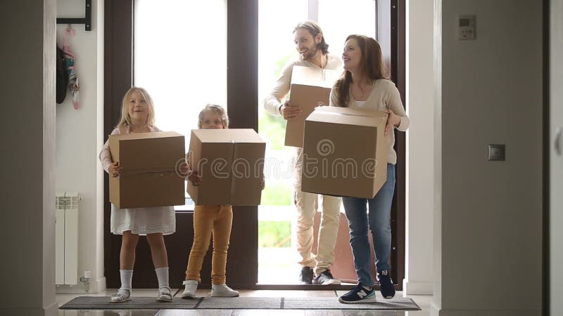 Familia feliz con los niños que sostienen la casa que entra de la puerta de abertura de las cajas