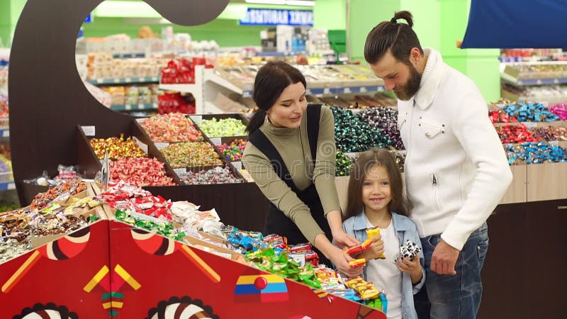Familia feliz con un caramelo y los dulces de la compra del niño en el supermercado Cámara lenta metrajes Familia feliz con un caramelo y los dulces de la compra del niño en el supermercado Cámara lenta metrajes