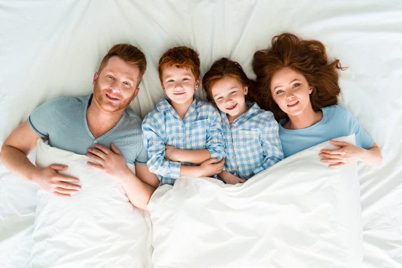 Familia feliz del pelirrojo en los pijamas que mienten en cama y la sonrisa fotografía de archivo