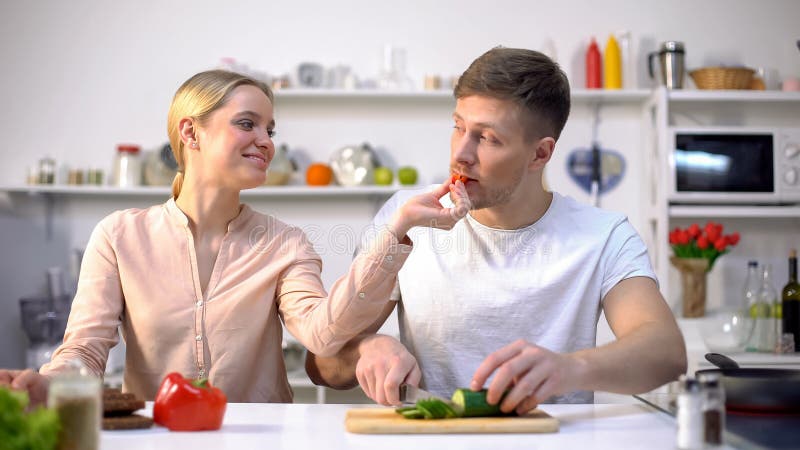 Familia feliz joven que liga, marido de alimentación con las verduras crudas, comida de la esposa del eco foto de archivo libre de regalías Familia feliz joven que liga, marido de alimentación con las verduras crudas, comida de la esposa del eco foto de archivo libre de regalías