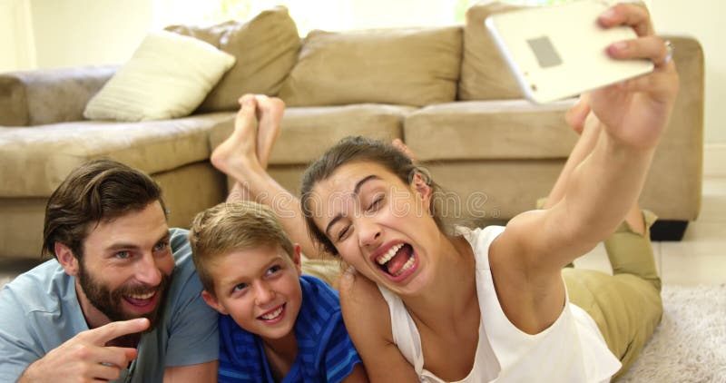 Familia feliz que miente en la alfombra que toma un selfie