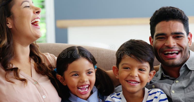 Familia feliz que se sienta en el sofá y que ríe en sala de estar