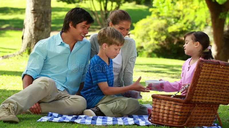 Familia feliz que se sienta en una manta durante una comida campestre