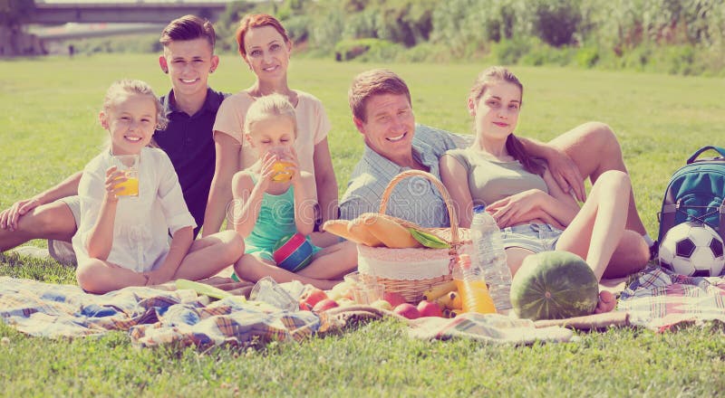Familia grande feliz de seis que tiene comida campestre en césped verde en parque imágenes de archivo libres de regalías Familia grande feliz de seis que tiene comida campestre en césped verde en parque imágenes de archivo libres de regalías