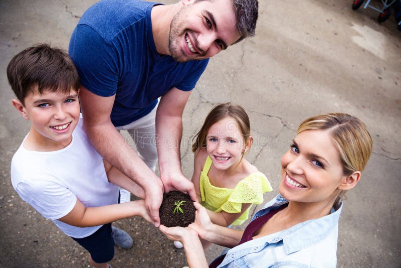 Familia hermosa que mira la cámara mientras que sostiene una planta en el invernadero foto de archivo libre de regalías Familia hermosa que mira la cámara mientras que sostiene una planta en el invernadero foto de archivo libre de regalías