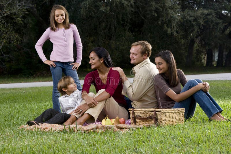 Familia interracial de cinco que tienen comida campestre en parque