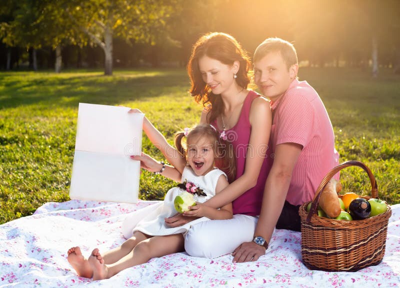 Familia joven feliz que tiene comida campestre en el prado foto de archivo Familia joven feliz que tiene comida campestre en el prado foto de archivo