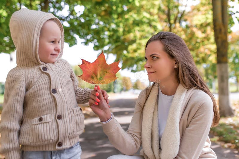 Familia joven, mamá sostiene la hoja de otoño, hijo pequeño sonriendo feliz con aspecto Emociones alegría, sonrisa y relajación fotografía de archivo libre de regalías Familia joven, mamá sostiene la hoja de otoño, hijo pequeño sonriendo feliz con aspecto Emociones alegría, sonrisa y relajación fotografía de archivo libre de regalías