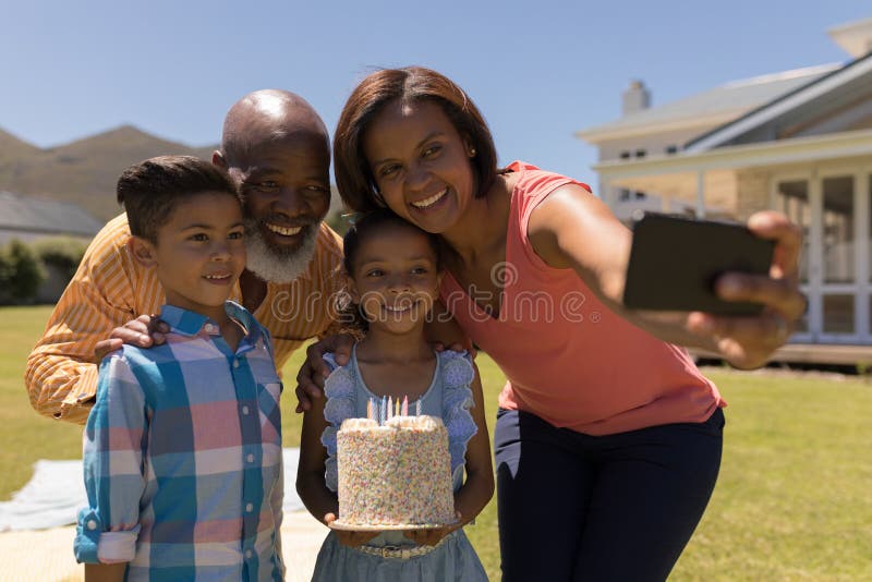 Familia multigeneración que toma el selfie con el teléfono móvil mientras que celebra el cumpleaños del grandaughter fotografía de archivo libre de regalías Familia multigeneración que toma el selfie con el teléfono móvil mientras que celebra el cumpleaños del grandaughter fotografía de archivo libre de regalías
