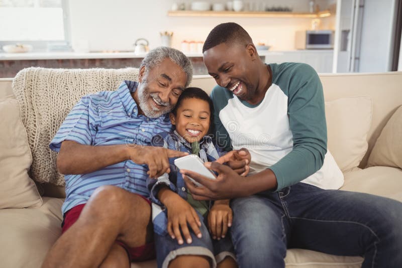 Familia multigeneración sonriente usando el teléfono móvil en sala de estar fotografía de archivo