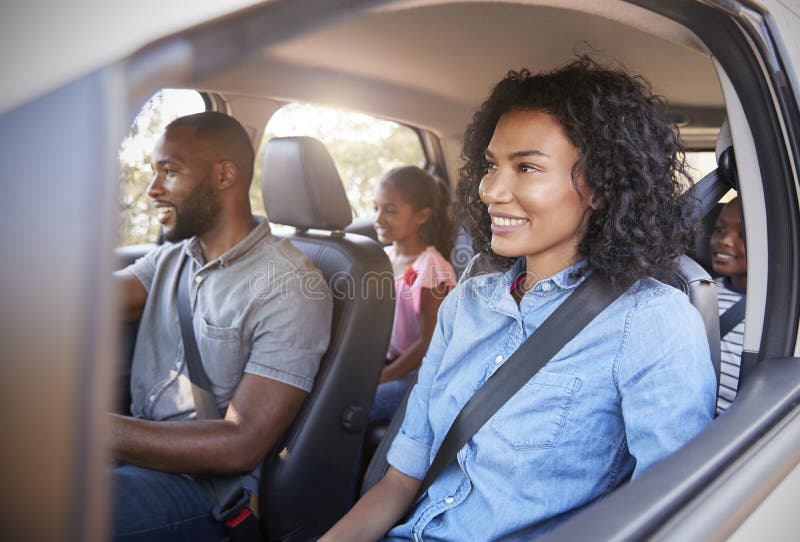 Familia negra joven con los niños en un coche que va en viaje por carretera