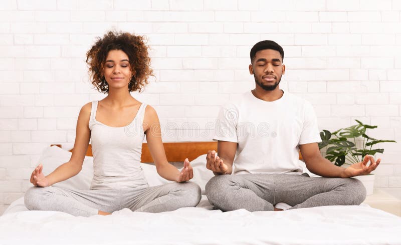 Familia negra joven que medita en cama junto imagenes de archivo Familia negra joven que medita en cama junto imagenes de archivo