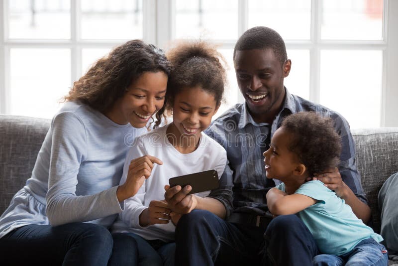 Familia negra y niños que ríen el vídeo divertido de observación en el teléfono fotos de archivo