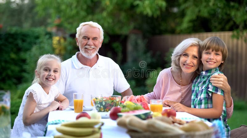 Familia que cena junto al aire libre y que mira la cámara, confiada sobre futuro fotografía de archivo libre de regalías Familia que cena junto al aire libre y que mira la cámara, confiada sobre futuro fotografía de archivo libre de regalías